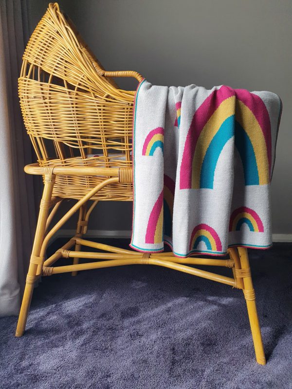 Merino wool Rainbow Baby Blanket in bright colours, draped over a rattan bassinet