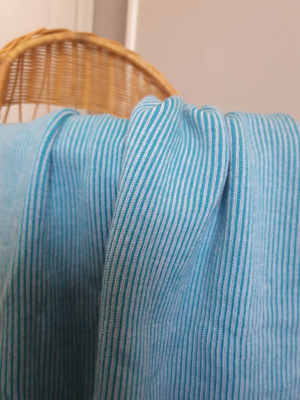 Aqua Bobbi Merino Wool Blanket in bright aqua and pale blue mix, close-up draped over a rattan bassinet.