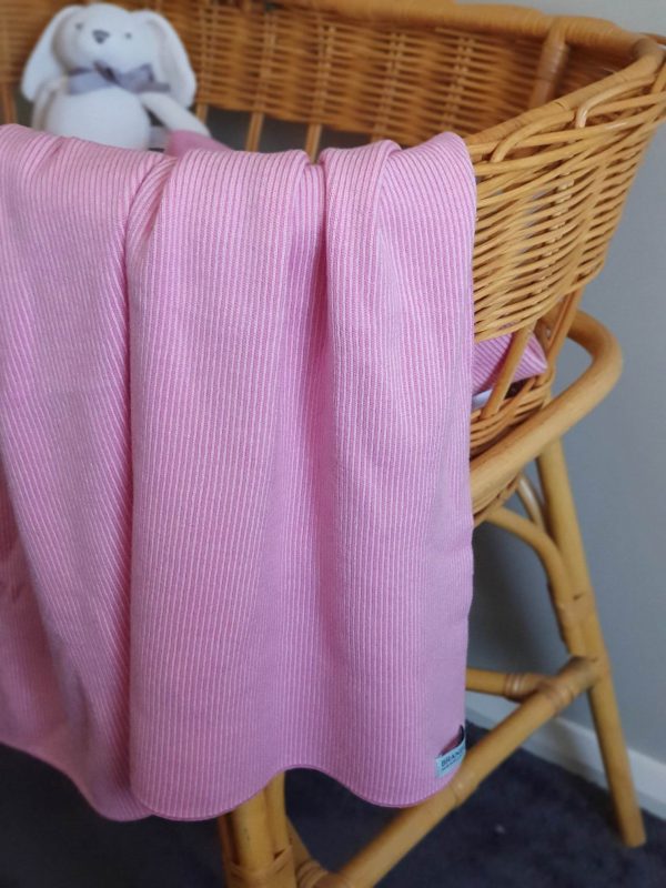 Taffy Bobbi Merino Wool Blanket in bright pink and pale pink mix, close-up draped over a rattan baby bassinet.