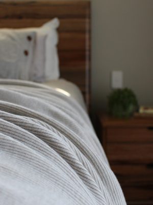 Australian Merino Wool Blanket - Bobbi in Cashew draped over a bed with a mini stripe design in light beige and white