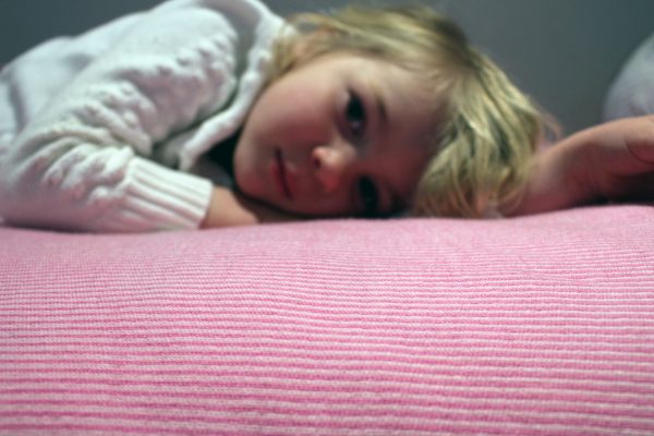 Taffy Merino Wool Blanket in bright pink and pale pink mix, close-up with a girl laying on top, showcasing its softness and comfort.