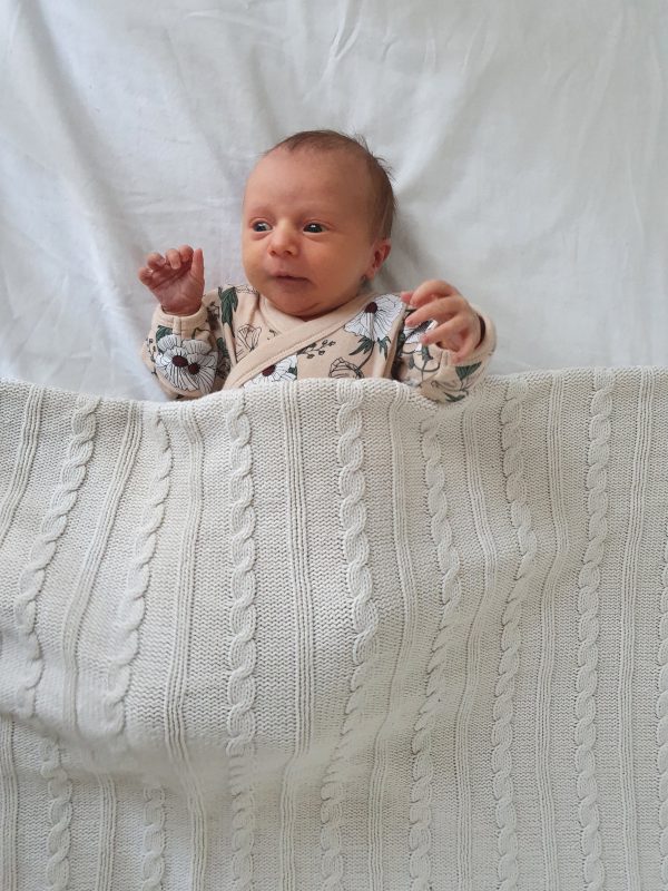 A baby in her cot all tucked in under an Branberry Australian Made, Cotton and Merino wool blend Cable Blanket in Milk White