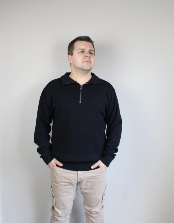 A man standing indoors wearing an Australian Made, pure merino woollen Branberry knitted jumper with zip neck in Black.