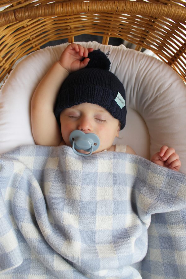Pale Blue and White Gingham Blanket made from Pure Australian Merino Wool. Baby wrapped snuggly in a bassinet, peacefully sleeping, wearing our navy Frankie wool baby beanie.