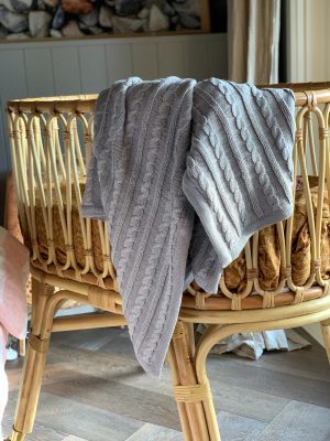 able Knit Blanket in Grey - Light grey blanket draped over an elegant cane bassinet, crafted with an exquisite blend of wool and cotton yarn. Timeless style for nurseries or homewares, 100% Australian made for longevity.