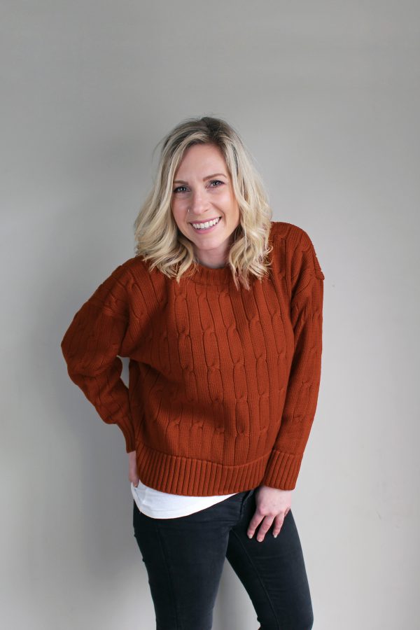 A lady wearing an Australian Made, Branberry merino wool cable crop, crew neck jumper in Rust