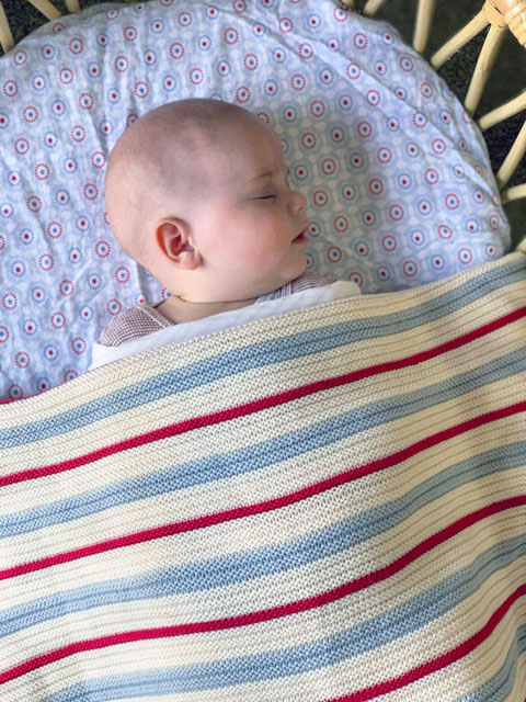 Blue, Red, and White Striped Garter Blanket made from a luxurious blend of cotton and wool. Close-up view showcasing the intricate stripes. Baby peacefully sleeping, wrapped in the cosy blanket.