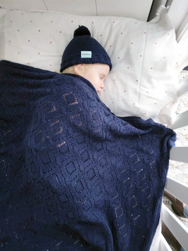 Branberry Heirloom Blanket in Princeton, a baby serenely sleeping in a cot with the matching Pure Wool Frankie Beanie