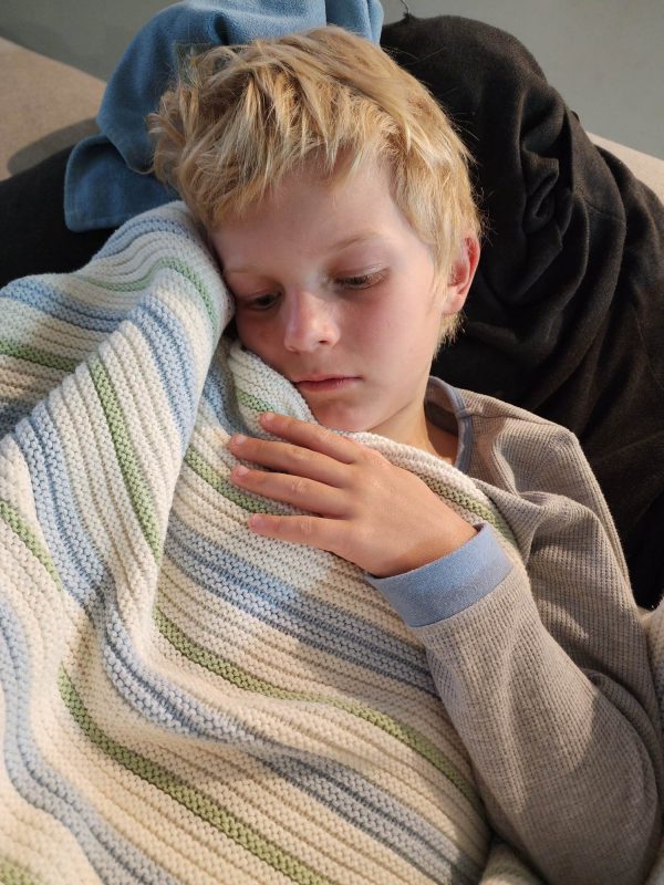 Striped Garter Blanket in Blue, Mint, and White, an image of a 10-year-old boy cuddling his blanket while sleeping
