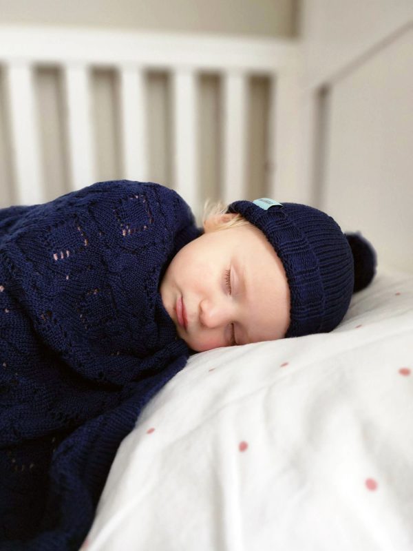 Branberry Heirloom Blanket in Princeton, a baby peacefully sleeping while swaddled in the blanket and wearing a matching Pure Wool Frankie Beanie.