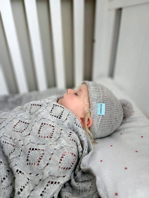 Branberry Heirloom Blanket in Smoke, a baby peacefully sleeping while swaddled in the blanket and wearing a matching Pure Wool Frankie Beanie.