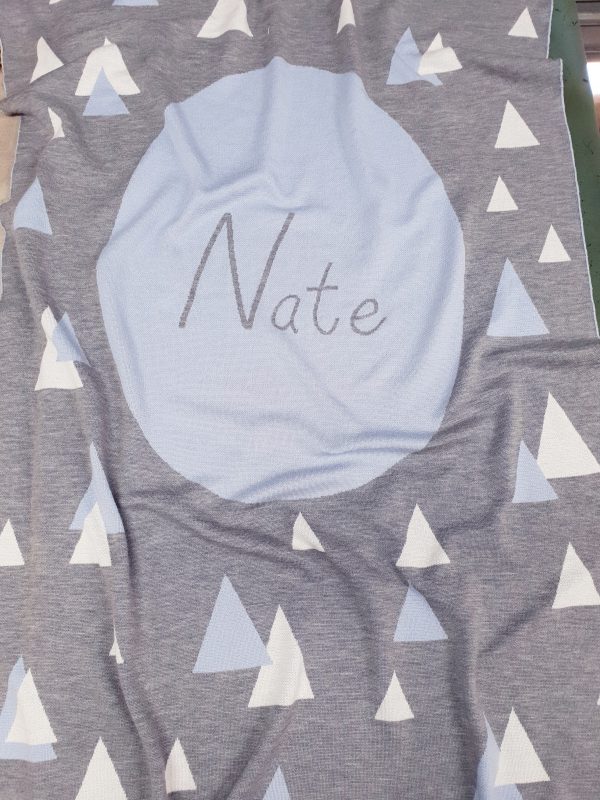 A Personalised Name Blanket with sporadic triangles with a big circle in the centre with a custom name, in a grey, blue and white colour combo, product photo. Made from Pure Australian Merino Wool and Made in Australia.