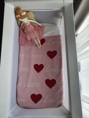 A bassinet set up with a fairy doll and a pure merino wool, personalised love hearts blanket in a pink, raspberry and white colour combo.