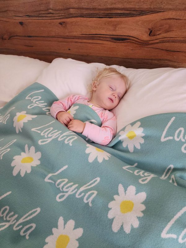 A baby sleeping under a Personalised Name Blanket with Daisy flowers in a Seafoam green colour. Made from Pure Australian Merino Wool and Made in Australia.