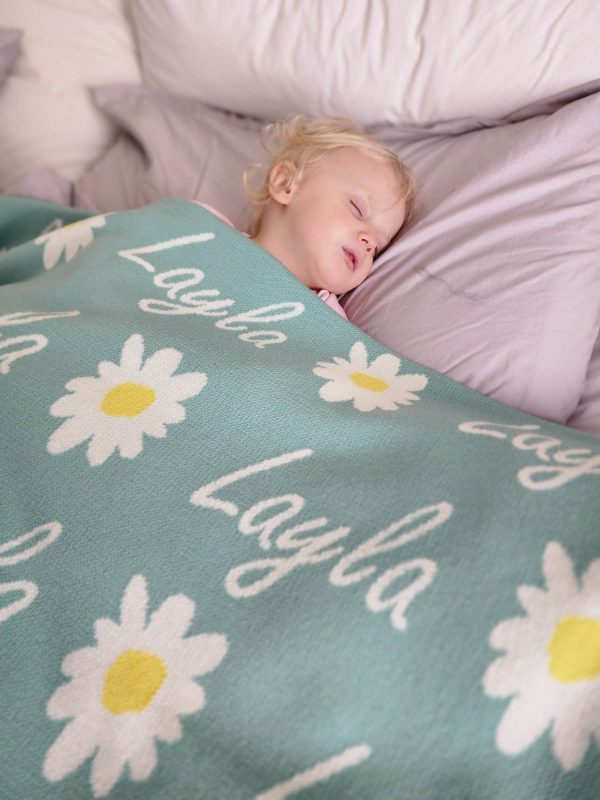 A baby sleeping under a Personalised Name Blanket with Daisy flowers in a Seafoam green colour. Made from Pure Australian Merino Wool and Made in Australia.
