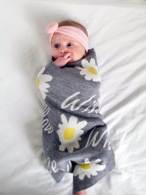 A baby swaddled with a Personalised Name Blanket with Daisy flowers in a Silver grey colour. Made from Pure Australian Merino Wool and Made in Australia.