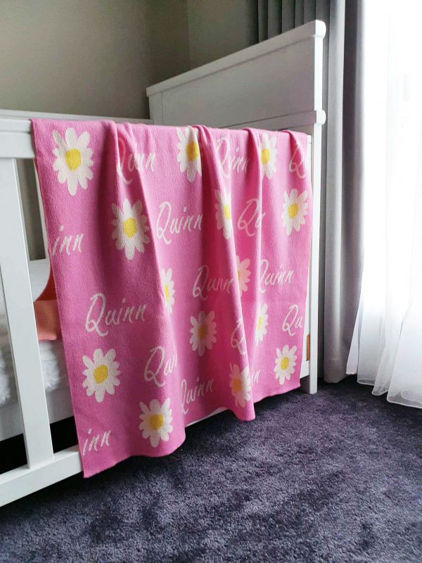 Lively Taffy Pink Personalised Daisy Name Blanket draping over a cot edge. Crafted from Pure Australian Merino Wool, proudly Made in Australia.