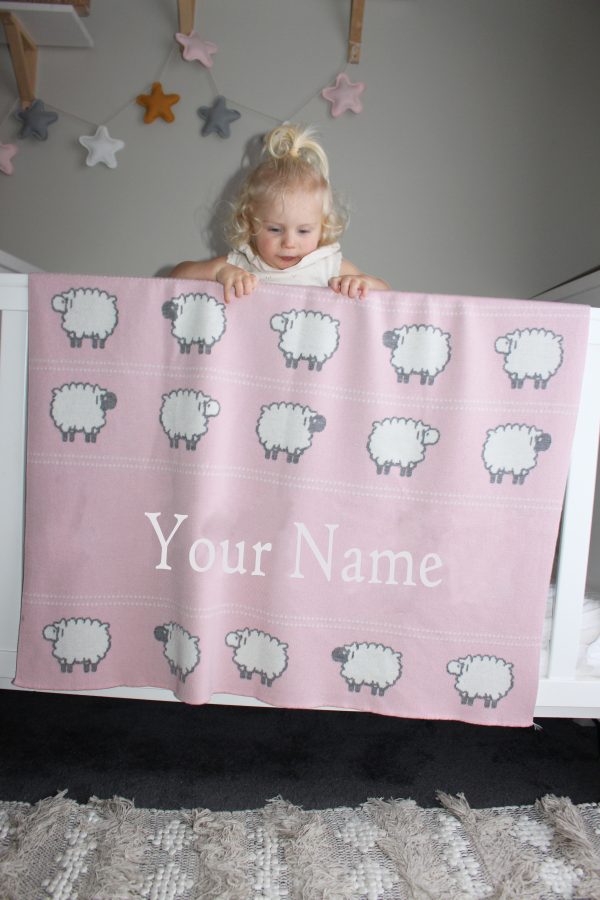 A toddler leaning on her Personalised Pure Australian Merino wool Sheep blanket in Pink, that's placed over a cot