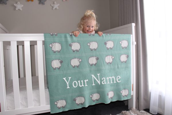 A toddler leaning on her Personalised Pure Australian Merino wool Sheep blanket in Seafoam Green, that's placed over a cot