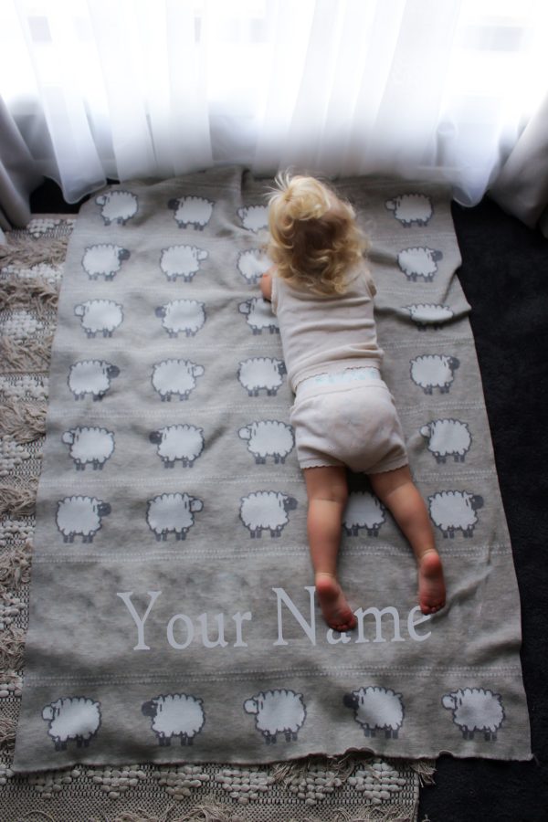 A toddler laying on top of a Personalised Pure Australian Merino wool Sheep blanket in light Grey.
