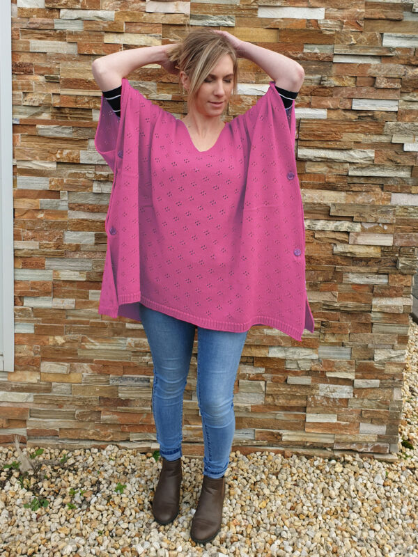 A woman tying her hair while wearing the Musk Pink Harlow Merino Wool Poncho, exuding effortless charm.