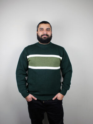 A man standing and wearing the Forest Noah Striped Jumper, a moss stitch knitted pullover in forest green with olive green and white stripes across the chest.