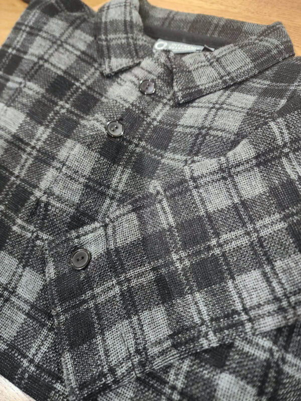 Close-up of a folded grey and black Woolly Camper shirt jumper showcasing its soft wool-nylon blend and check pattern.