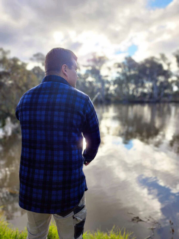 Man fishing at dusk in a lake, wearing the blue and black Woolly Camper shirt jumper.